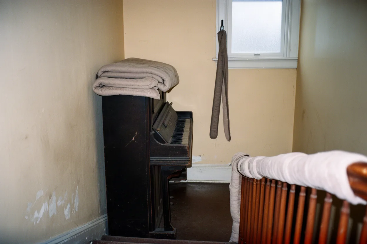 A blanket-wrapped upright piano on a tight stairwell landing mid-move